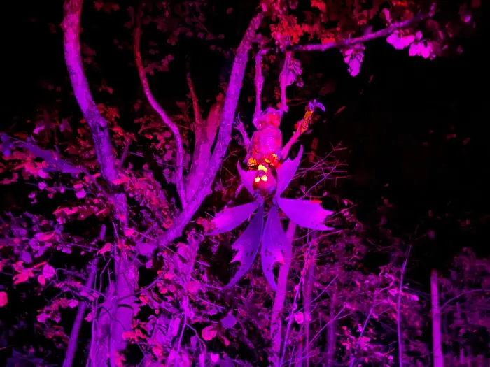A creature suspended among trees under purple lighting