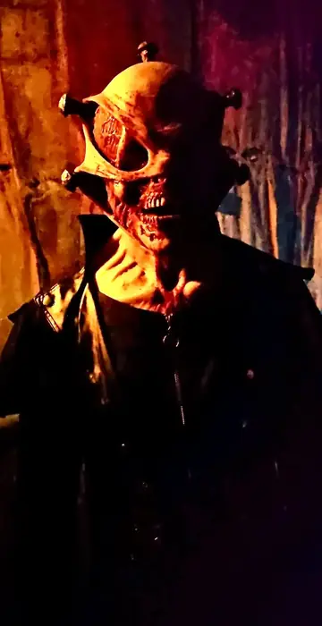 A masked Grimm Grounds scare actor under dramatic lighting