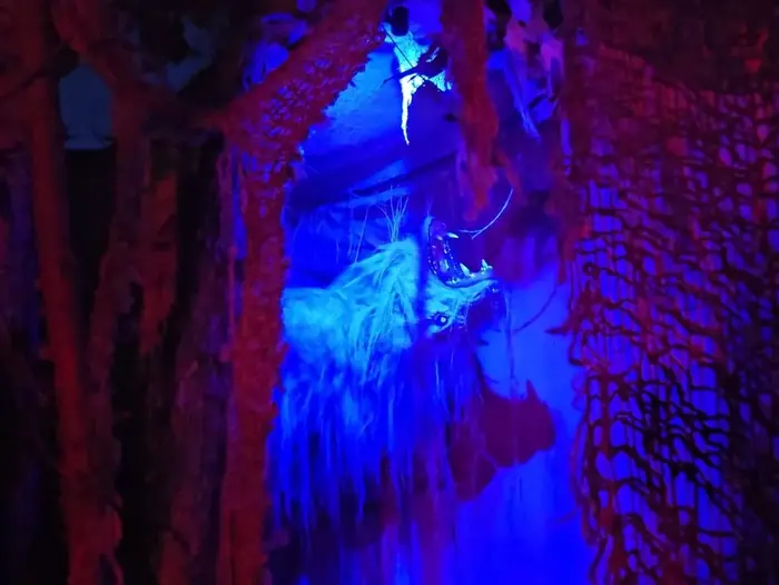 A blue-lit creature tucked behind tattered fabric