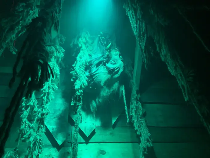 A creature emerging through hanging fabric in green light